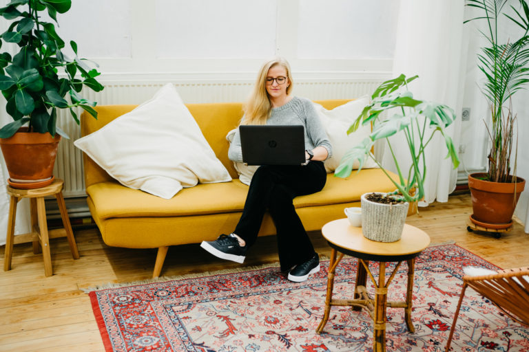 Lauren Van Noten, Notion expert, zittend op een gele sofa met haar laptop in een huiselijke, lichte ruimte.