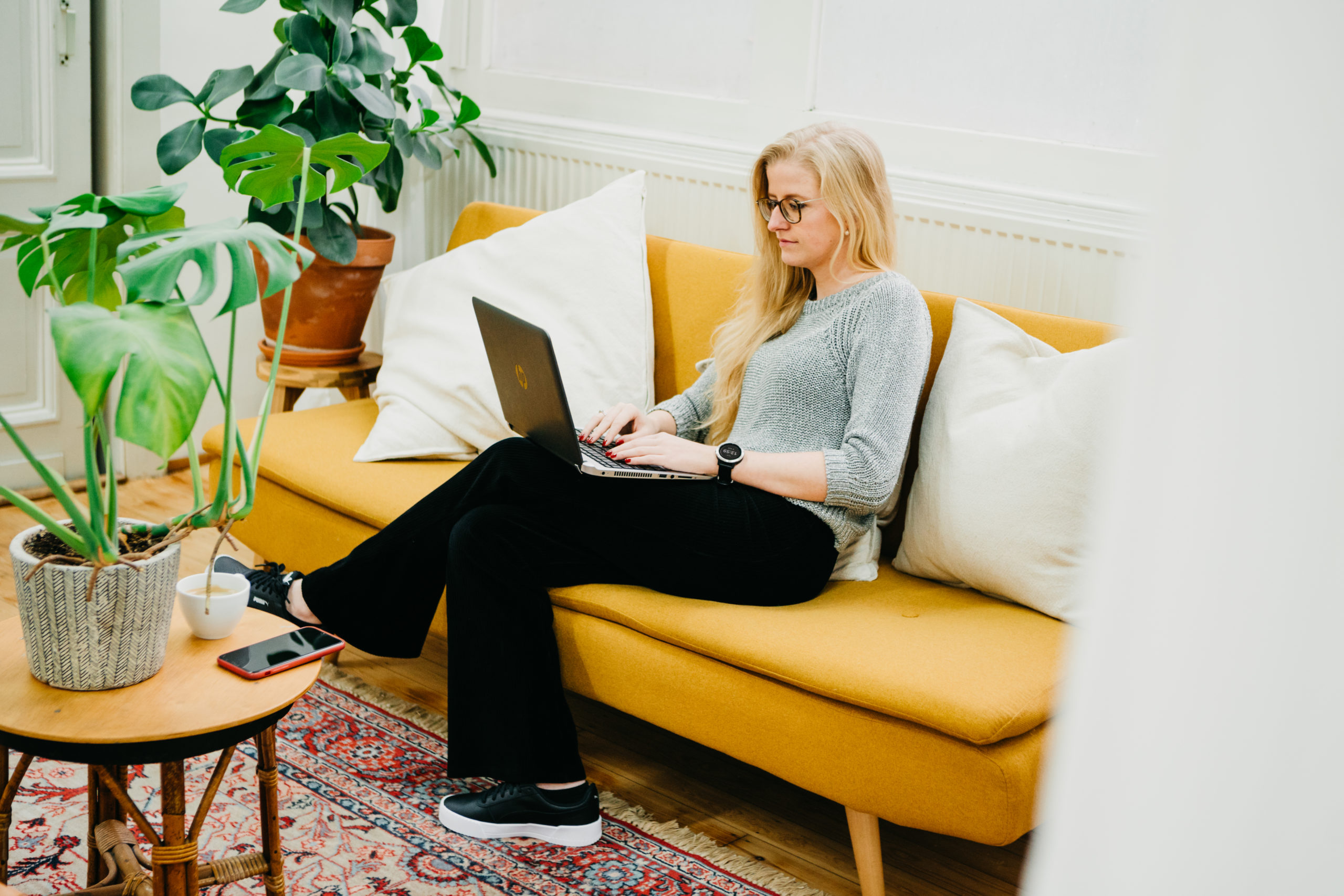 Lauren Van Noten werkt aan een houten tafel op haar laptop, naast een plant.