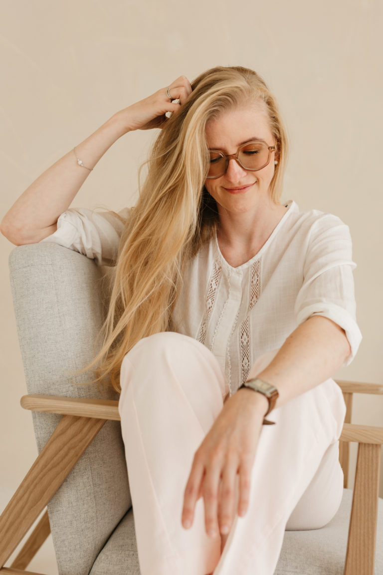 Lauren Van Noten zittend in een lichte fauteuil, met haar hand in haar haar en haar benen ontspannen opgetrokken.