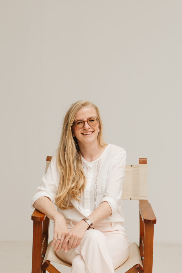 Lauren Van Noten, Notion expert, lachend zittend op een houten stoel in een lichte studio.