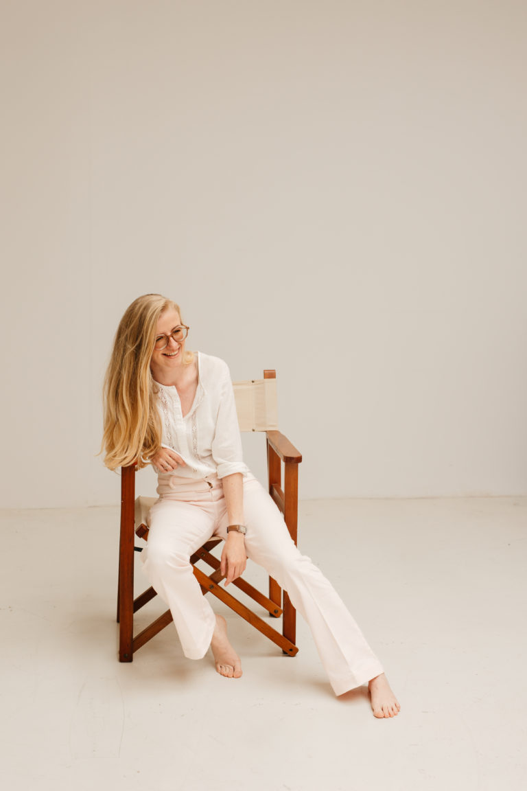 Lauren Van Noten, Notion expert, ontspannen zittend op een houten stoel in een minimalistische studio.